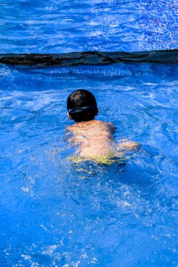 Havuzda yüzen mutlu Hintli çocuk, sıcak yaz tatillerinde hava tüpüyle birlikte yüzen çocuk, büyük bir havuzda yüzen çocuk..