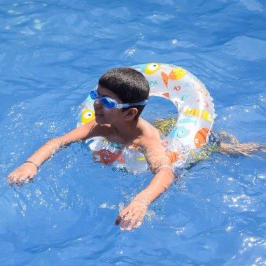 Havuzda yüzen mutlu Hintli çocuk, sıcak yaz tatillerinde hava tüpüyle birlikte yüzen çocuk, büyük bir havuzda yüzen çocuk..