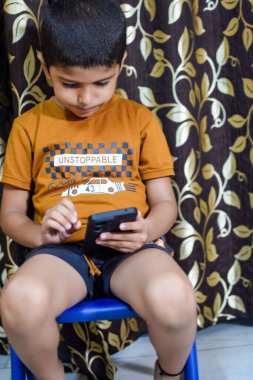 Evde cep telefonu kullanan Asyalı mutlu küçük çocuğun portresi. Küçük çocuk elinde cep telefonu tutuyor, internetten okul konseptine geri dönüyor. Çevrimiçi Sınıf kavramı