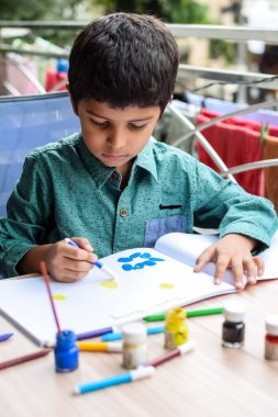 Zeki Hintli küçük çocuk yaz tatillerinde farklı renklerde su rengi setiyle baş parmak boyası yapıyor, şirin Hintli çocuk ahşap masaya renkli başparmak resimleri çiziyor.