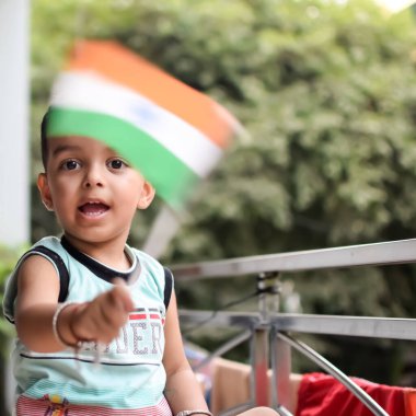 Evinin balkonunda asılı duran Kızılderili bayrağını tutan sevimli Hintli çocuk. Ulusal bayrağıyla masada oturan mutlu çocuğun parlak portresi