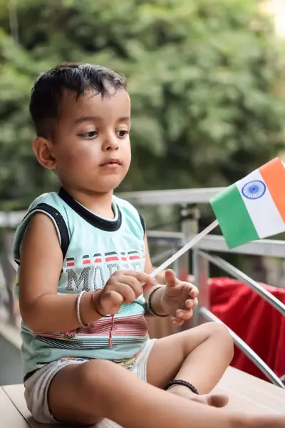 stock image Cute Indian boy holding Indian National Flag in his hangs at home balcony. Bright portrait of happy child sitting on the table with national flag