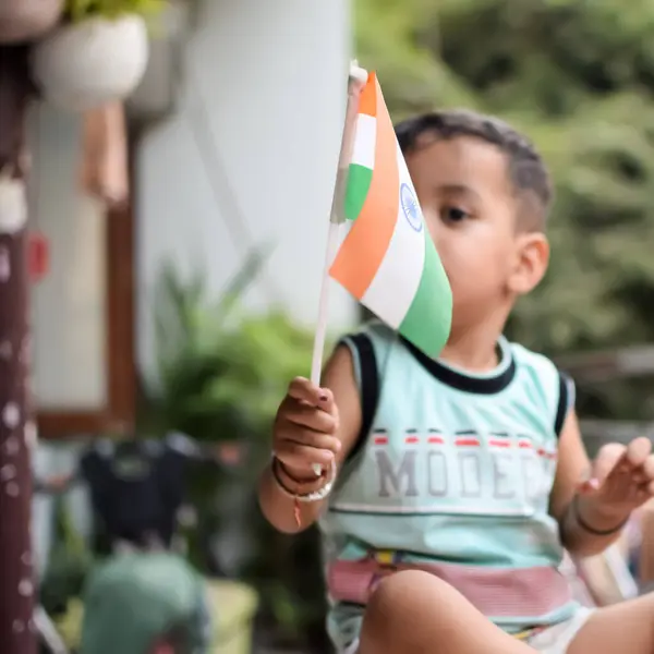 stock image Cute Indian boy holding Indian National Flag in his hangs at home balcony. Bright portrait of happy child sitting on the table with national flag