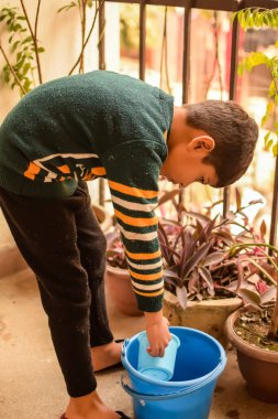 Şirin 5 yaşındaki Asyalı çocuk, ev balkonundaki saksıları suluyor. Bitkileri sularken küçük tatlı bir çocuğun doğaya olan sevgisi.