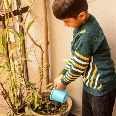 Şirin 5 yaşındaki Asyalı çocuk, ev balkonundaki saksıları suluyor. Bitkileri sularken küçük tatlı bir çocuğun doğaya olan sevgisi.