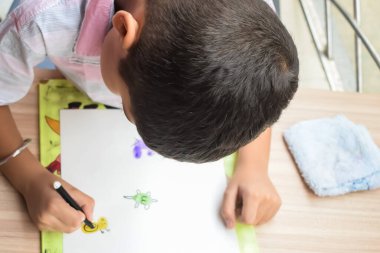 Zeki Hintli küçük çocuk yaz tatillerinde farklı renklerde su rengi setiyle baş parmak boyası yapıyor, şirin Hintli çocuk ahşap masaya renkli başparmak resimleri çiziyor.