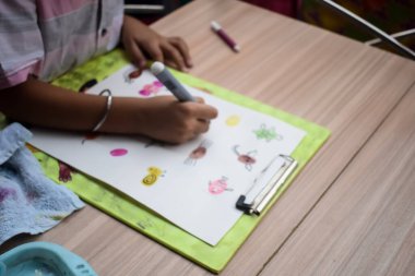 Zeki Hintli küçük çocuk yaz tatillerinde farklı renklerde su rengi setiyle baş parmak boyası yapıyor, şirin Hintli çocuk ahşap masaya renkli başparmak resimleri çiziyor.