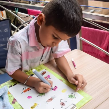 Zeki Hintli küçük çocuk yaz tatillerinde farklı renklerde su rengi setiyle baş parmak boyası yapıyor, şirin Hintli çocuk ahşap masaya renkli başparmak resimleri çiziyor.