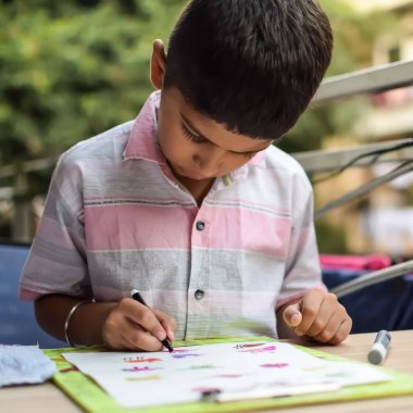 Zeki Hintli küçük çocuk yaz tatillerinde farklı renklerde su rengi setiyle baş parmak boyası yapıyor, şirin Hintli çocuk ahşap masaya renkli başparmak resimleri çiziyor.