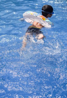 Havuzda yüzen mutlu Hintli çocuk, sıcak yaz tatillerinde hava tüpüyle birlikte yüzen çocuk, büyük bir havuzda yüzen çocuk..