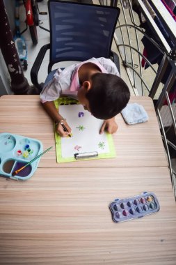 Zeki Hintli küçük çocuk yaz tatillerinde farklı renklerde su rengi setiyle baş parmak boyası yapıyor, şirin Hintli çocuk ahşap masaya renkli başparmak resimleri çiziyor.