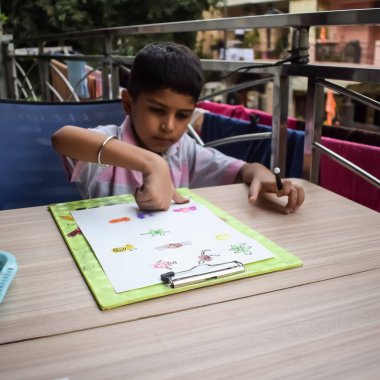 Zeki Hintli küçük çocuk yaz tatillerinde farklı renklerde su rengi setiyle baş parmak boyası yapıyor, şirin Hintli çocuk ahşap masaya renkli başparmak resimleri çiziyor.