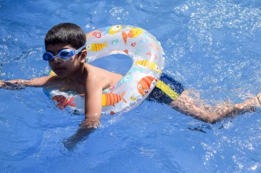 Havuzda yüzen mutlu Hintli çocuk, sıcak yaz tatillerinde hava tüpüyle birlikte yüzen çocuk, büyük bir havuzda yüzen çocuk..