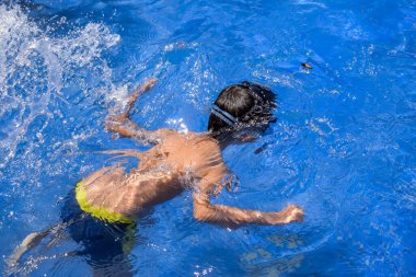 Havuzda yüzen mutlu Hintli çocuk, sıcak yaz tatillerinde hava tüpüyle birlikte yüzen çocuk, büyük bir havuzda yüzen çocuk..