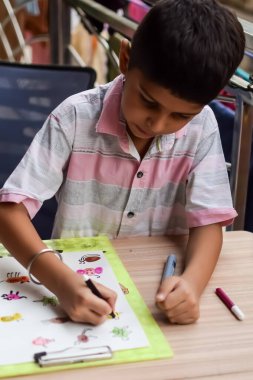 Zeki Hintli küçük çocuk yaz tatillerinde farklı renklerde su rengi setiyle baş parmak boyası yapıyor, şirin Hintli çocuk ahşap masaya renkli başparmak resimleri çiziyor.