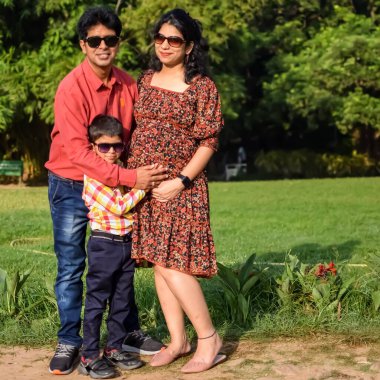 Hintli çift 5 yaşındaki çocuklarıyla hamilelik çekimleri için poz veriyor. Çift yeşil çimenli bir çimenlikte poz veriyor ve kadın Yeni Delhi, Hindistan 'daki Lodhi Garden' da bebeğiyle hava atıyor.