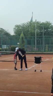 Delhi, Hindistan, 16 Nisan 2025 - Genç tenisçiler kil tenis kortunda antrenörlük yapıyor, küçük tenis oyuncuları yaklaşan turnuva için antrenman yapıyor