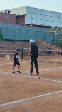 Delhi, Hindistan, 16 Nisan 2025 - Genç tenisçiler kil tenis kortunda antrenörlük yapıyor, küçük tenis oyuncuları yaklaşan turnuva için antrenman yapıyor