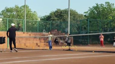 Delhi, Hindistan, 16 Nisan 2025 - Genç tenisçiler kil tenis kortunda antrenörlük yapıyor, küçük tenis oyuncuları yaklaşan turnuva için antrenman yapıyor