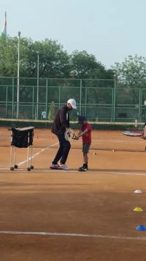 Delhi, Hindistan, 16 Nisan 2025 - Genç tenisçiler kil tenis kortunda antrenörlük yapıyor, küçük tenis oyuncuları yaklaşan turnuva için antrenman yapıyor
