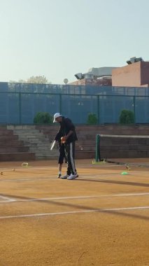 Delhi, Hindistan, 16 Nisan 2025 - Genç tenisçiler kil tenis kortunda antrenörlük yapıyor, küçük tenis oyuncuları yaklaşan turnuva için antrenman yapıyor