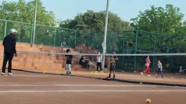 Delhi, Hindistan, 16 Nisan 2025 - Genç tenisçiler kil tenis kortunda antrenörlük yapıyor, küçük tenis oyuncuları yaklaşan turnuva için antrenman yapıyor