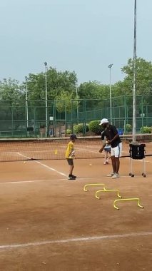 Delhi, Hindistan, 16 Nisan 2025 - Genç tenisçiler kil tenis kortunda antrenörlük yapıyor, küçük tenis oyuncuları yaklaşan turnuva için antrenman yapıyor