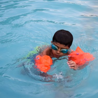 Havuzda yüzen mutlu Hintli çocuk, sıcak yaz tatillerinde hava tüpüyle birlikte yüzen çocuk, büyük bir havuzda yüzen çocuk..