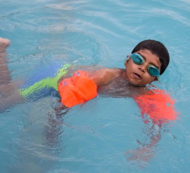 Havuzda yüzen mutlu Hintli çocuk, sıcak yaz tatillerinde hava tüpüyle birlikte yüzen çocuk, büyük bir havuzda yüzen çocuk..