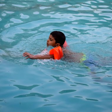 Havuzda yüzen mutlu Hintli çocuk, sıcak yaz tatillerinde hava tüpüyle birlikte yüzen çocuk, büyük bir havuzda yüzen çocuk..
