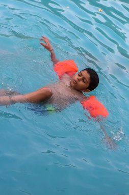 Havuzda yüzen mutlu Hintli çocuk, sıcak yaz tatillerinde hava tüpüyle birlikte yüzen çocuk, büyük bir havuzda yüzen çocuk..