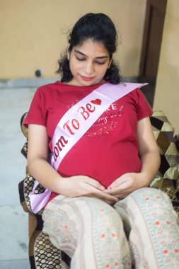 Hamile bir Hintli kadın hamilelik çekimleri için poz veriyor ve ellerini karnının üstüne koyuyor, Hintli hamile kadın elini karnına koyuyor ve evinde hamile elbisesi var.