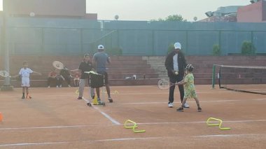 Delhi, Hindistan, 17 Şubat 2025 - Maha Open için kil tenis kortunda antrenörlük yapan genç tenisçiler, yaklaşan turnuva için küçük tenis oyuncuları antrenman yapıyor