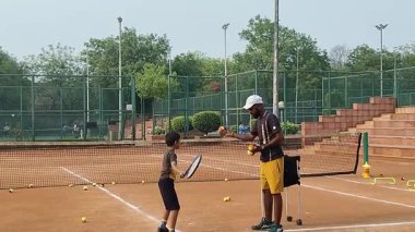 Delhi, Hindistan, 17 Şubat 2025 - Maha Open için kil tenis kortunda antrenörlük yapan genç tenisçiler, yaklaşan turnuva için küçük tenis oyuncuları antrenman yapıyor