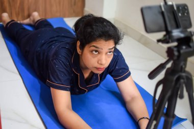 Evde yoga yapan genç Hintli bir kadın çevrimiçi yoga seansında güzel bir kız temel yoga pozisyonunda Asyalı bir kadın kapalı alanda yoga yapıyor.