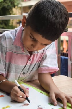 Zeki Hintli küçük çocuk yaz tatillerinde farklı renklerde su rengi setiyle baş parmak boyası yapıyor, şirin Hintli çocuk ahşap masaya renkli başparmak resimleri çiziyor.