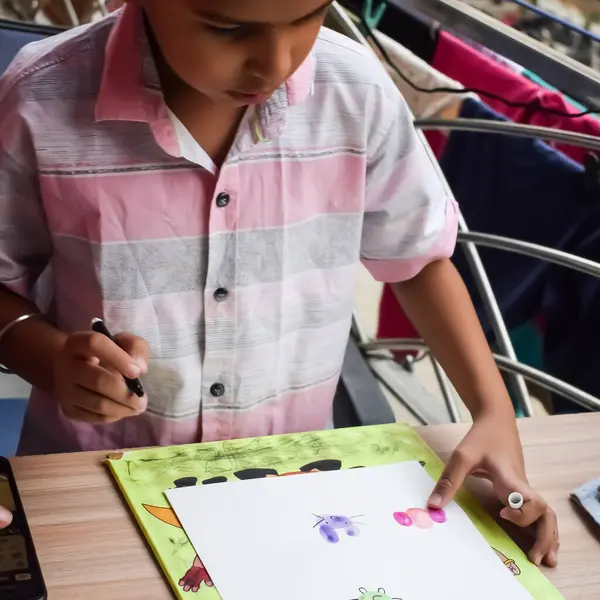 Zeki Hintli küçük çocuk yaz tatillerinde farklı renklerde su rengi setiyle baş parmak boyası yapıyor, şirin Hintli çocuk ahşap masaya renkli başparmak resimleri çiziyor.