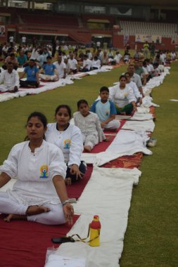 Yeni Delhi, Hindistan, 21 Haziran 2025 - Uluslararası Yoga Günü 'nde Delhi' deki Yamuna Spor Kompleksi 'nde grup Yoga egzersiz oturumu, kriket stadyumunda yoga sınıfına katılan büyük bir grup yetişkin