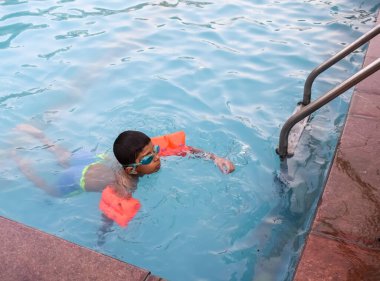 Havuzda yüzen mutlu Hintli çocuk, sıcak yaz tatillerinde hava tüpüyle birlikte yüzen çocuk, büyük bir havuzda yüzen çocuk..