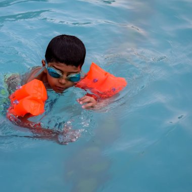 Havuzda yüzen mutlu Hintli çocuk, sıcak yaz tatillerinde hava tüpüyle birlikte yüzen çocuk, büyük bir havuzda yüzen çocuk..