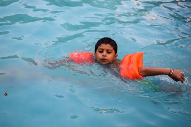 Havuzda yüzen mutlu Hintli çocuk, sıcak yaz tatillerinde hava tüpüyle birlikte yüzen çocuk, büyük bir havuzda yüzen çocuk..