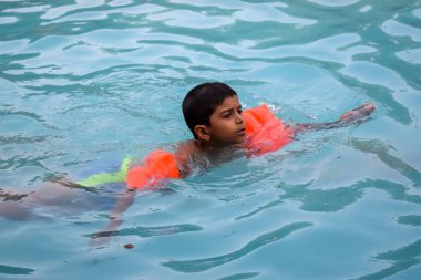 Havuzda yüzen mutlu Hintli çocuk, sıcak yaz tatillerinde hava tüpüyle birlikte yüzen çocuk, büyük bir havuzda yüzen çocuk..