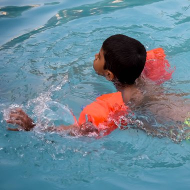 Havuzda yüzen mutlu Hintli çocuk, sıcak yaz tatillerinde hava tüpüyle birlikte yüzen çocuk, büyük bir havuzda yüzen çocuk..