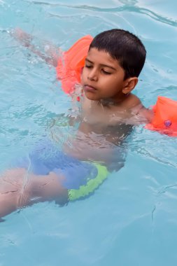 Havuzda yüzen mutlu Hintli çocuk, sıcak yaz tatillerinde hava tüpüyle birlikte yüzen çocuk, büyük bir havuzda yüzen çocuk..