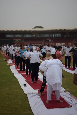 Yeni Delhi, Hindistan, 21 Haziran 2025 - Uluslararası Yoga Günü 'nde Delhi' deki Yamuna Spor Kompleksi 'nde grup Yoga egzersiz oturumu, kriket stadyumunda yoga sınıfına katılan büyük bir grup yetişkin