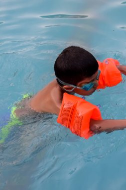 Havuzda yüzen mutlu Hintli çocuk, sıcak yaz tatillerinde hava tüpüyle birlikte yüzen çocuk, büyük bir havuzda yüzen çocuk..