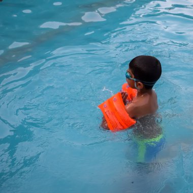 Havuzda yüzen mutlu Hintli çocuk, sıcak yaz tatillerinde hava tüpüyle birlikte yüzen çocuk, büyük bir havuzda yüzen çocuk..
