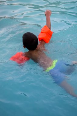 Havuzda yüzen mutlu Hintli çocuk, sıcak yaz tatillerinde hava tüpüyle birlikte yüzen çocuk, büyük bir havuzda yüzen çocuk..