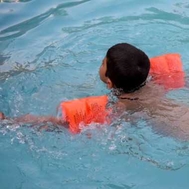 Havuzda yüzen mutlu Hintli çocuk, sıcak yaz tatillerinde hava tüpüyle birlikte yüzen çocuk, büyük bir havuzda yüzen çocuk..