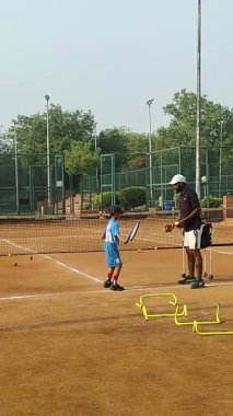 Delhi, Hindistan, 17 Şubat 2025 - Maha Open için kil tenis kortunda antrenörlük yapan genç tenisçiler, yaklaşan turnuva için küçük tenis oyuncuları antrenman yapıyor